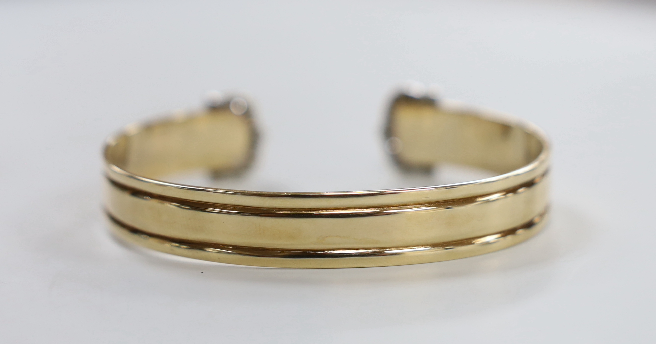 A yellow metal and diamond chip cluster set open work bangle, interior diameter approx. 66mm, gross weight 23.3 grams.